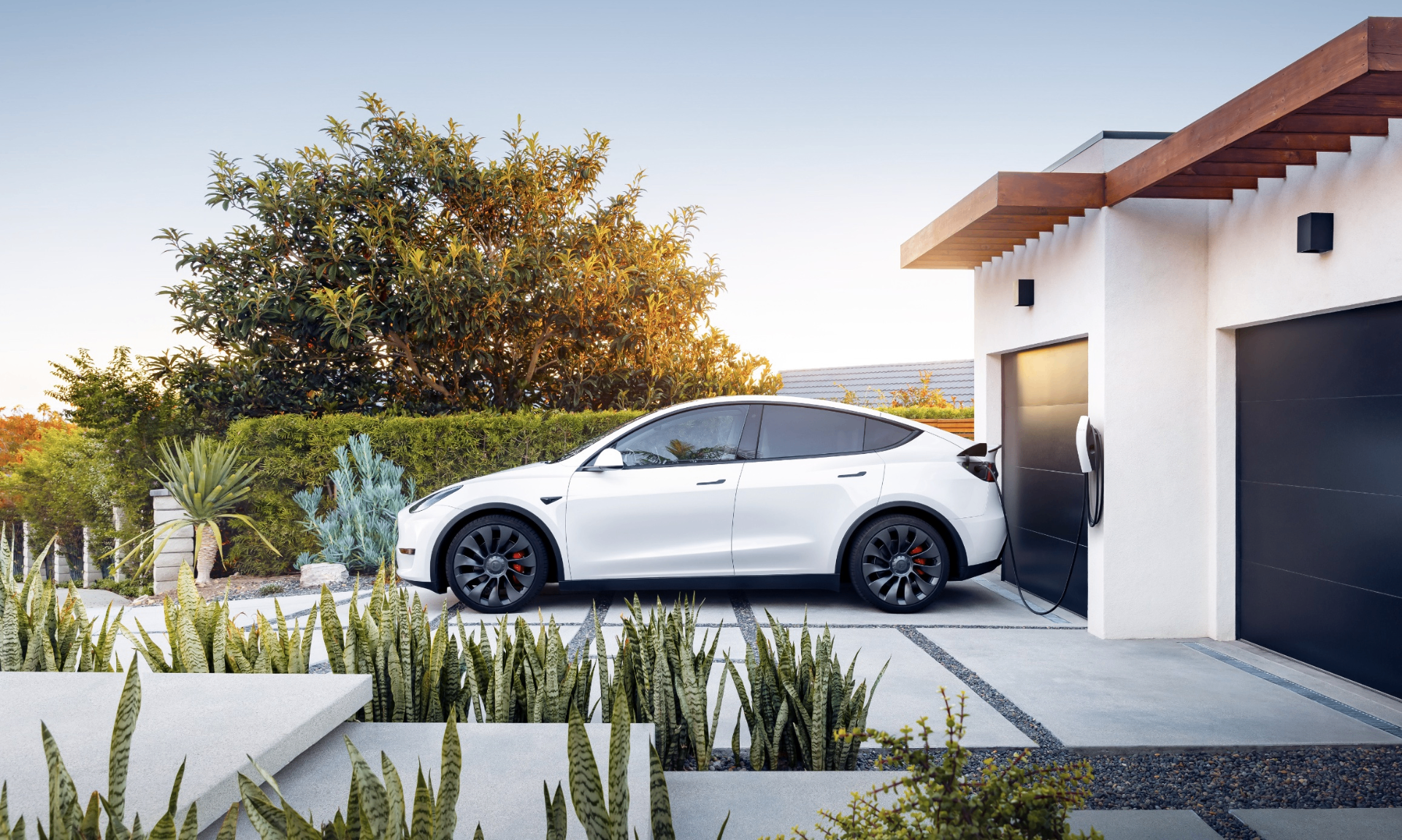 Tesla Model Y charging at home in a modern driveway with Wall Connector