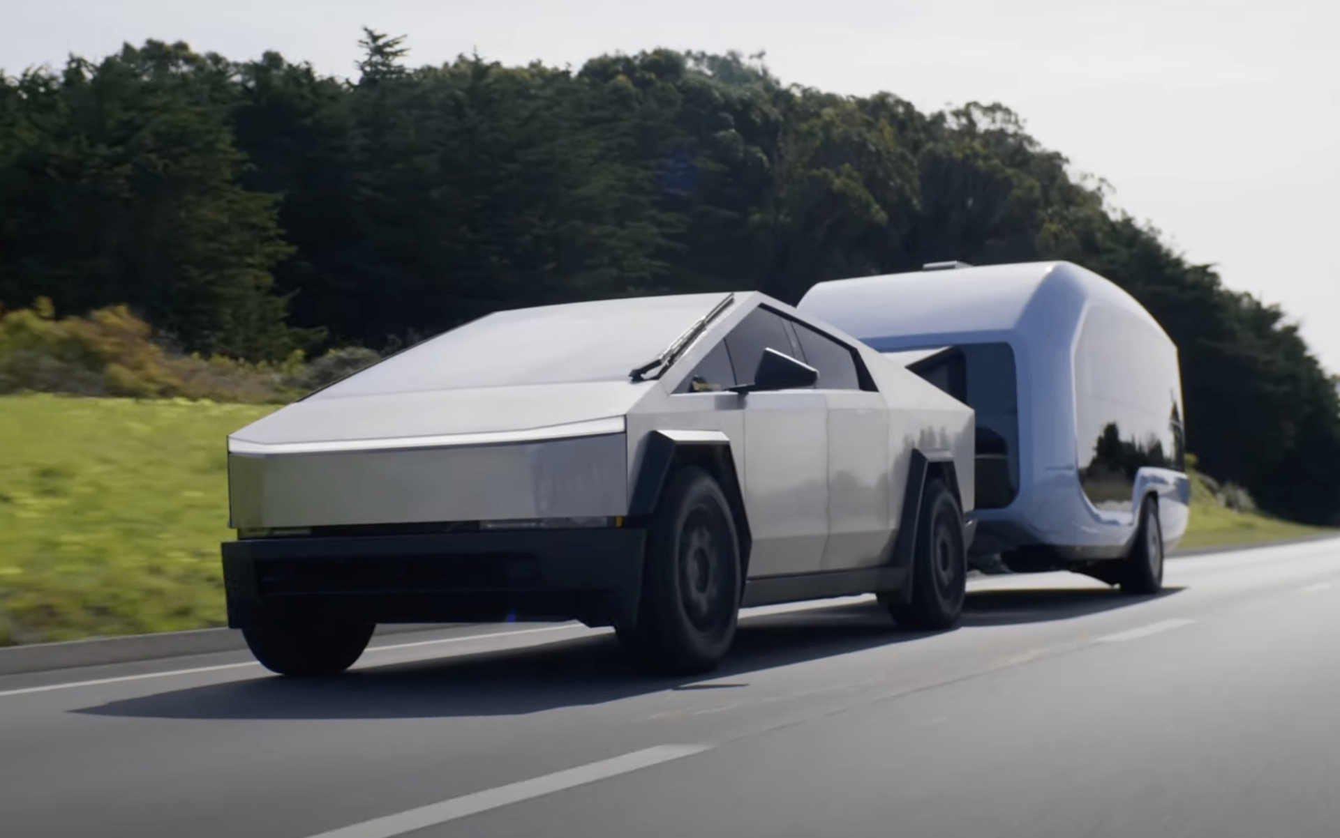 Tesla Cybertruck towing an aerodynamic silver travel trailer on a highway