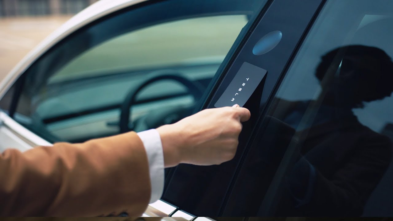 Hand holding a Tesla key card against a white Tesla door pillar